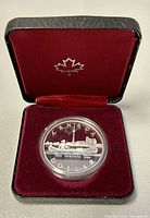 Silver $500 dollar coin commemorating 150th anniversary of Toronto inside original black presentation box with burgundy velvet lining and Royal Canadian Mint maple leaf on lid.