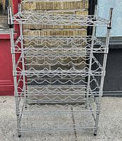 Front view of the stainless steel wine rack showing five tiers with wavy bottle holders and four supporting poles.