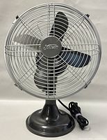 Front view of the Sunbeam fan showing the circular metal protective grill, three black blades, and the Sunbeam center badge on the grill with power cord coiled beside the base.