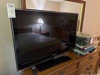 Photo showing front view of the Hughes flat-screen TV on a stand with remote underneath.