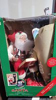 Photo showing Santa Claus statue seated with pipe and list inside original green box with clear window.