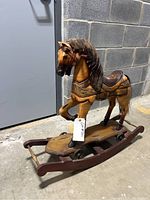 Front left perspective of antique wooden rocking horse showing detailed painting, saddle, mane and rocker base with metal wheels.