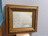 Photo showing square antique wall mirror with decorative carved wood frame and reflective glass surface.