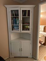 Full view of the white wooden corner cabinet showing upper glass doors, middle open shelf, and lower solid doors.