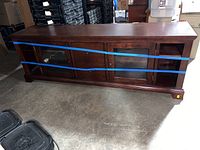 Front view of the wooden TV stand credenza showing glass doors and multiple drawers with blue tape across the front for transport security.