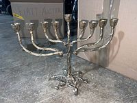 Metal menorah with nine branches for candles on a concrete floor with gray background.