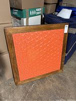 Photo of the game table showing its orange textured top and wooden border, standing on the floor leaning against stacked boxes and other furniture.