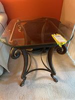 Wrought iron end table with curled leg design and glass top from an angled view.