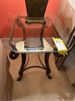Wrought iron end table with a rectangular clear glass top showing curved legs and dark metal finish.