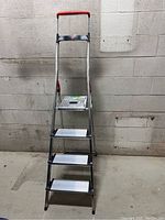 Front view of the Hailo metal ladder showing four steps including the top platform and red handle grip.