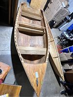 Photo showing two handmade wooden canoes, the larger one featuring cross seats, visible wood grain, and a metal latch on bow, smaller canoe next to it