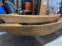 Side view of two stacked wooden canoes, showing size difference and construction style.