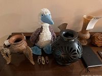 Group of assorted decorative items including plush dodo toy, carved pottery vase, pottery vessel, small wooden items, and notebook