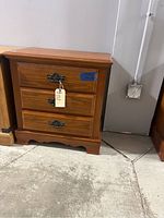 Front view of the wood nightstand with three drawers and decorative metal handles showing the overall condition and design.