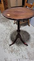 Full view of round wooden side table with scalloped edge top and tripod pedestal base.