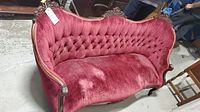 Full view of a Victorian-style red velvet sofa with carved wooden frame and button-tufted backrest, showing wear and discoloration.