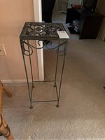 Front view of the wrought iron plant stand showing its decorative square top and slender legs.