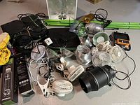 Overall lot showing black Vivosun 5x5 grow tent, multiple small fans (clip and pedestal), silver ducting hose, black inline duct fan, aluminum reflectors, power cords, two 1000W grow light bulbs (MH and HPS), and metal frame poles scattered on the floor