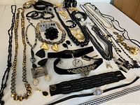 Overview of the black and gold costume jewelry laid on white surface. Includes multiple necklaces, chokers, bracelets, earrings, and pins with glass bead components and velvet accents.