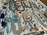 Top-down view showing a wide spread of blue and turquoise jewelry pieces including necklaces, bracelets, and earrings arranged across a table.