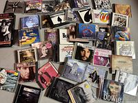 Top view photo showing a large assortment of CD cases scattered displaying various album covers including The Beatles Yellow Submarine, David Bowie, Rolling Stones, and others.