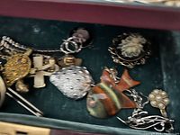 Close-up of first compartment showing safety-pin brooch, fish pendant, metallic cross and chains