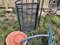 Black metal firewood rack with mesh center panel, weathered terracotta plant saucers, and parts of metal plant stands