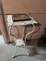Front side view showing the white metal frame, ornate top edge, and weathered wood top with measuring stick beside for scale.