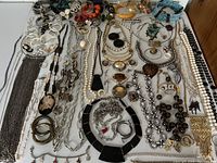 Wide view of assorted modern and vintage costume jewelry including chain necklaces, pearl beads, rhinestone and turquoise pieces, bangles, earrings, brooches, and pins spread out on a flat surface.