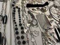 Wide view of various black and silver costume jewelry including necklaces, brooches, and earrings arranged on a white surface