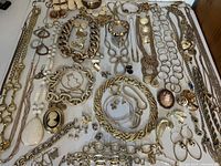 Overview photo showing the entire collection of gold tone costume jewelry including necklaces, bracelets, earrings, brooches, scarf/shoe clips, and ring laid out on a white surface.