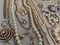 Close-up of left section showing faux pearl and chain necklaces, pearl drop earrings and brooches