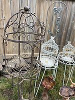 Photo of multiple metal outdoor garden accessories including birdcages, bird baths, Sheppard hook, trellis, and plant stands showing overall lot contents.
