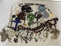 Collection displayed showing multiple rosaries with different bead materials and colors along with assorted crosses and crucifixes.