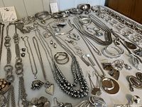 Wide overall view of silver-tone costume jewelry laid out showing necklaces, bracelets, earrings, brooches, and misc. items in a neat spread