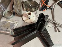 Close-up of black metal supports or brackets in front of metal sheet and light socket on floor.