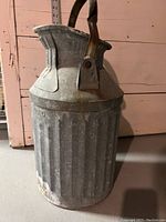 Side view of vintage galvanized metal jug showing ribbed design, handle, and spout with hinged cover.