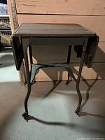 Front view of the vintage metal typewriter desk showing the fold-down side extensions and caster wheels.