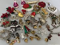 Top down image showing entire lot of 34 Christmas-themed costume jewelry pieces including brooches, pins, earrings, and a chain bracelet all laid out neatly