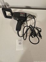 Black electric plug-in drill with D-handle grip and power cord coiled beside it.
