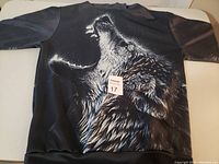 Black large hoodie with a howling wolf graphic on the front, laid flat on a surface shown from different angles.