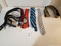 Photo showing two black leather belts with metal buckles and four neckties in various designs and colors on a white surface.