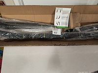 Opened box showing pull-up bar parts wrapped in bubble wrap with instruction manual.