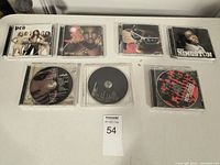 Photo of 7 music CDs in jewel cases, arranged in two rows on a flat surface showing album cover art and discs.