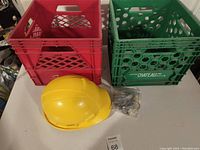 Photo showing two plastic crates (red and green), a yellow hard hat, and a bundle of telephone cords on floor.