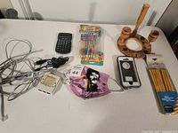 Photo of various items including calculator, earphones, power strip, face mask, phone case, pencils, wooden pipe stand, and pens.