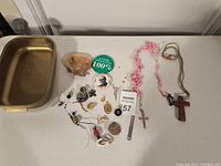 Photo of assorted small knickknacks including religious pendants, buttons, a brass tray, and decorative items, laid out on a white surface.