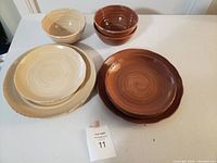 Photo shows 8 stoneware dishes including 4 bowls and 4 plates in beige and brown colors on white surface.