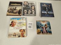 Photo of 5 DVDs and Blu-ray DVDs on a white surface showing cover art including Sons of Anarchy Season 1, Bones Season 4, Blue Bloods Season 1, The Impossible, and Let My People Go.