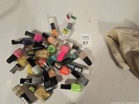 Photo showing various used nail polish bottles in multiple colors including pink, green, orange, gold, black and white among others on a white surface.